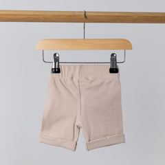 Back view of oat ribbed organic cotton kids shorts hanging on a wooden hanger, with neutral background.