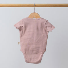 Dusty pink short sleeve baby bodysuit hanging from a wooden hanger, back view showing clean finishing and soft breathable cotton fabric.
