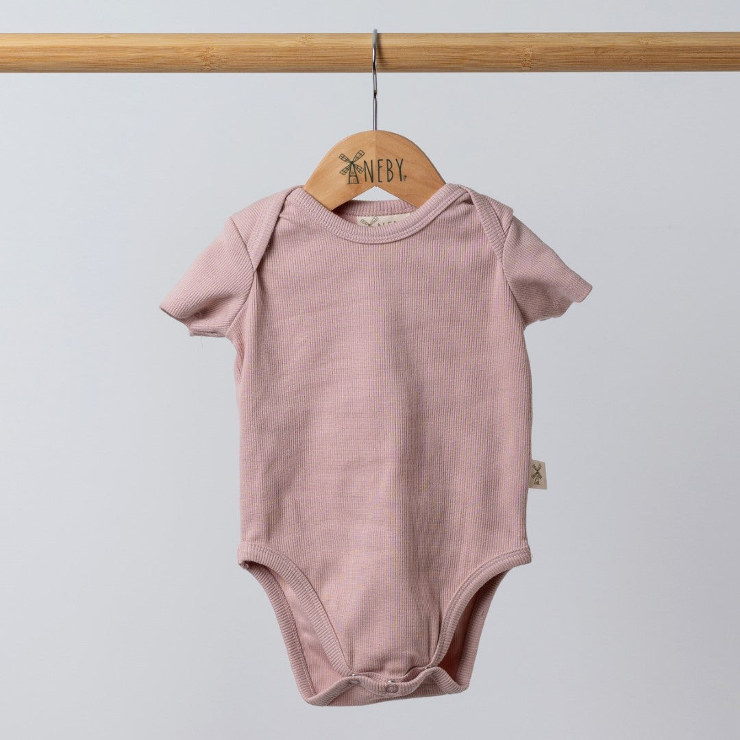 Dusty pink short sleeve baby bodysuit hanging on a wooden hanger, with visible Aneby label and envelope neckline for easy changes.