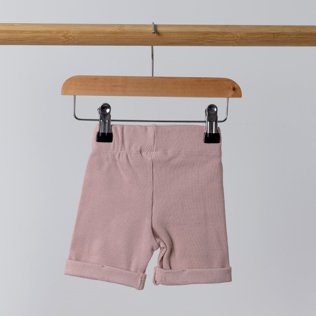 Back view of pink ribbed organic cotton kids shorts hanging on a wooden hanger, with neutral background.