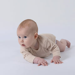 Baby wearing an oat-coloured ribbed bodysuit with long sleeves, looking at the camera with a soft expression.