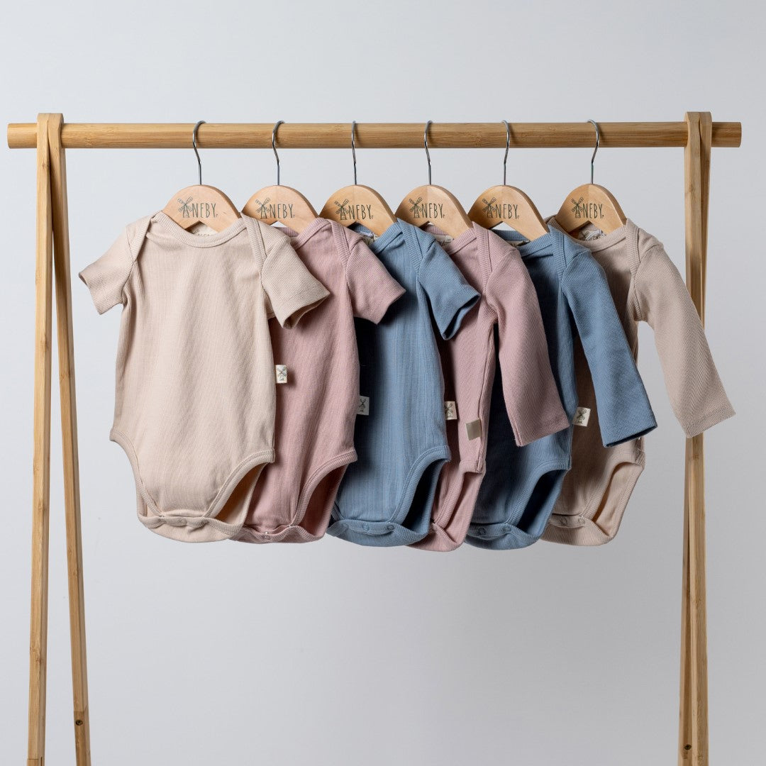 6 short sleeve and long sleeve baby bodysuits in oat, pink and blue on a wooden clothes rail