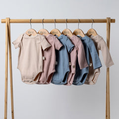 6 short sleeve and long sleeve baby bodysuits in oat, pink and blue on a wooden clothes rail