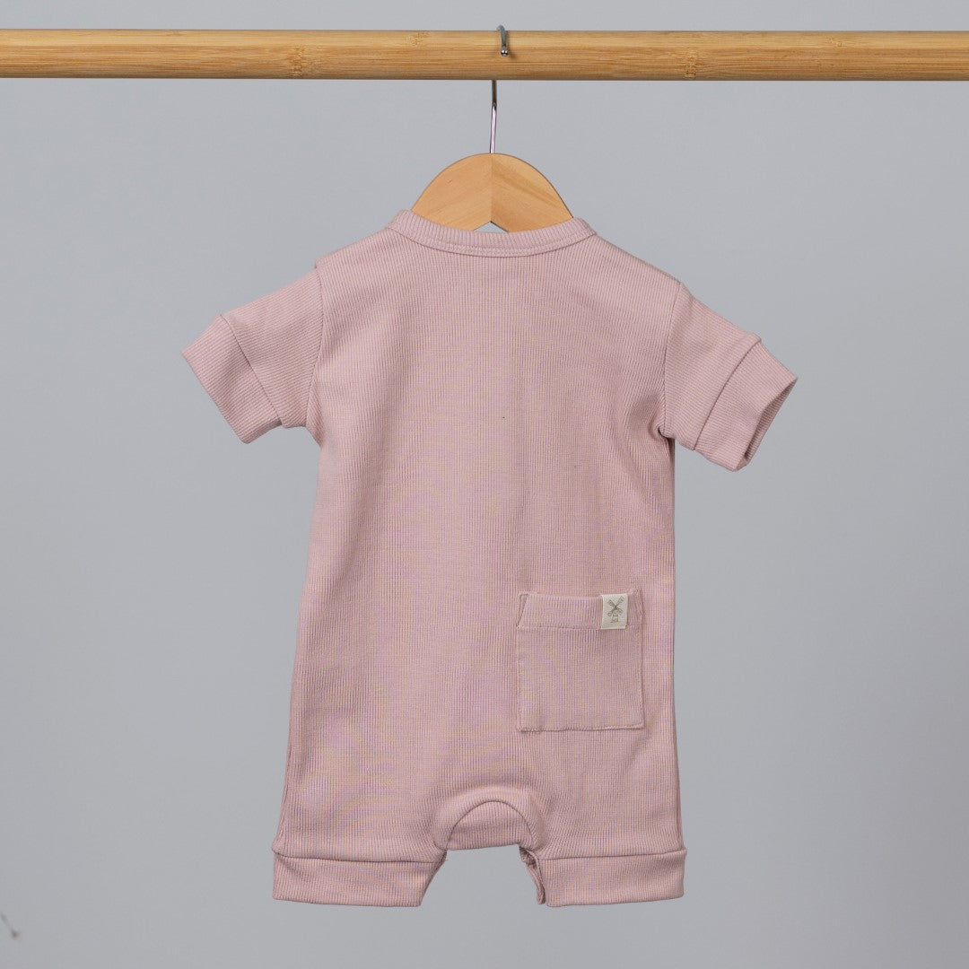 Dusty pink short sleeve rib baby romper hanging from wooden frame, with pocket and Aneby hem tag visible.