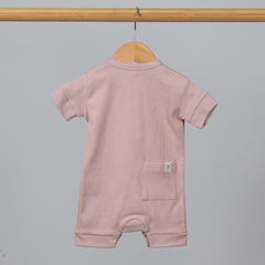 Dusty pink short sleeve rib baby romper hanging from wooden frame, with pocket and Aneby hem tag visible.